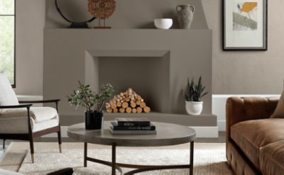 Living room with neutral colored furniture, round coffee table with decor, modern fireplace with logs and decor on mantle.